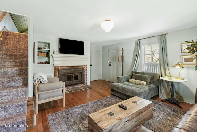 living room with built in shelves, a brick fireplace, baseboards, and wood finished floors