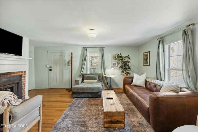 living room featuring a healthy amount of sunlight, a brick fireplace, baseboards, and wood finished floors