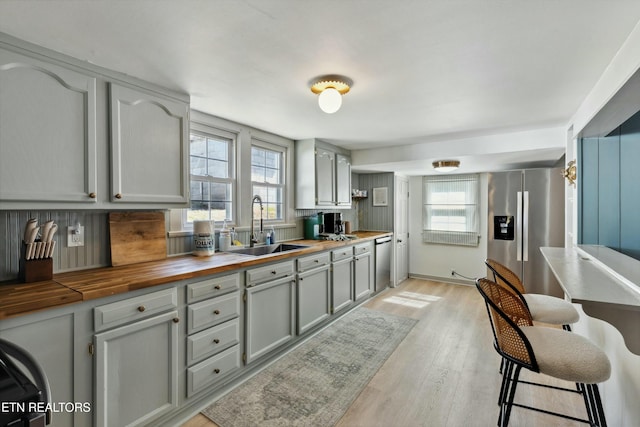 kitchen featuring stainless steel appliances, gray cabinets, light wood-style floors, a sink, and butcher block countertops