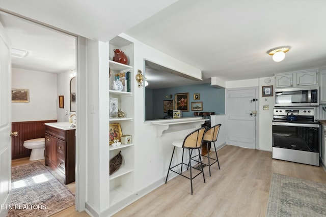 kitchen with stainless steel appliances, light wood-style floors, built in features, a kitchen breakfast bar, and open shelves