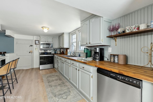 kitchen with open shelves, stainless steel appliances, butcher block counters, a sink, and light wood-type flooring