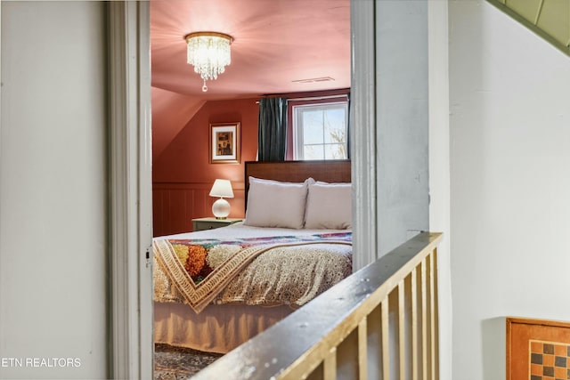 bedroom with lofted ceiling, an inviting chandelier, and a wainscoted wall