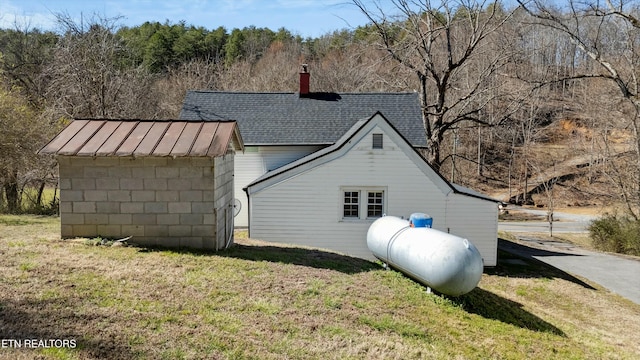 view of side of property with a storage shed, an outdoor structure, roof with shingles, a lawn, and a standing seam roof