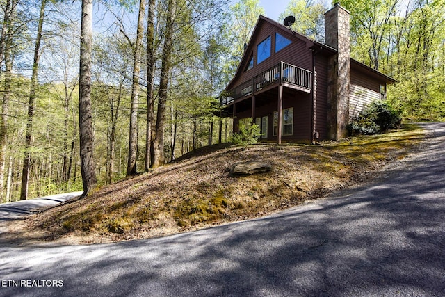 view of front facade featuring a deck, a chimney, and a view of trees