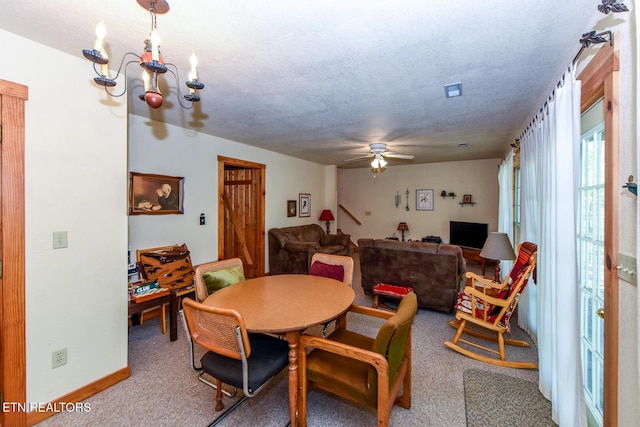 carpeted dining area featuring a textured ceiling, ceiling fan with notable chandelier, and baseboards