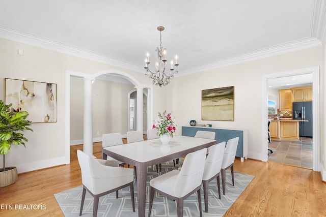 dining space featuring arched walkways, crown molding, decorative columns, light wood-style flooring, and baseboards