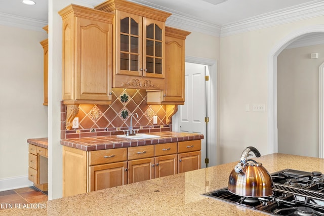 kitchen featuring arched walkways, tasteful backsplash, stovetop with downdraft, glass insert cabinets, and a sink