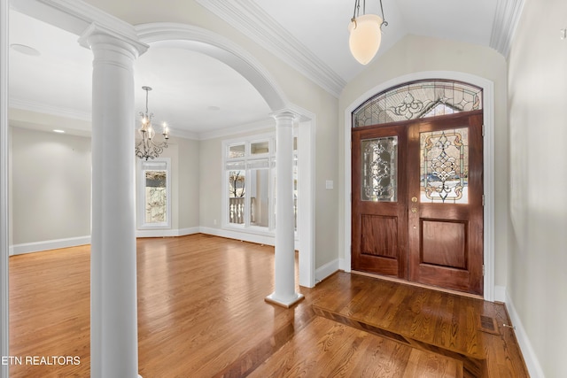 foyer entrance featuring wood finished floors, baseboards, vaulted ceiling, ornamental molding, and ornate columns