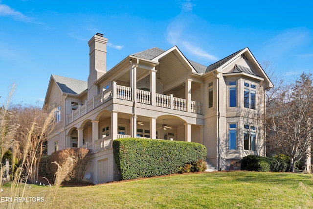 view of front facade with a chimney, stucco siding, a front yard, ceiling fan, and a balcony