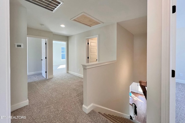 hall with carpet, visible vents, baseboards, and an upstairs landing