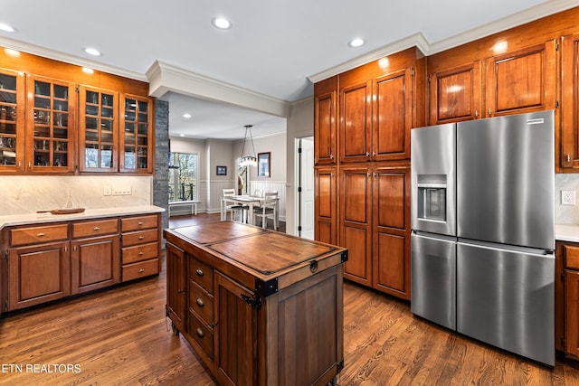 kitchen with dark wood-style floors, stainless steel fridge with ice dispenser, ornamental molding, glass insert cabinets, and backsplash