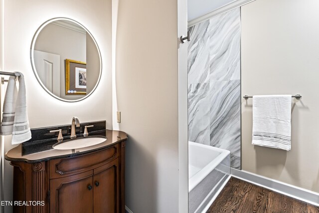 bathroom with vanity, wood finished floors, a tub to relax in, baseboards, and a shower