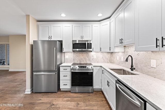 kitchen with light stone countertops, a sink, dark wood-type flooring, appliances with stainless steel finishes, and backsplash