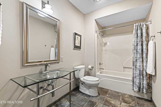 bathroom featuring toilet, stone finish floor, a sink, shower / bath combination with curtain, and baseboards