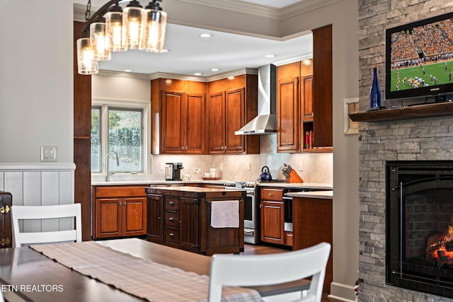 kitchen with a stone fireplace, stainless steel stove, light countertops, and wall chimney range hood