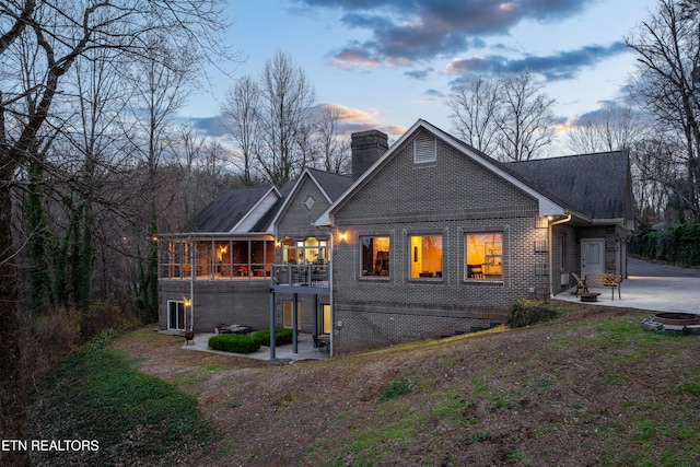 back of property at dusk featuring a patio area, a chimney, a fire pit, and brick siding