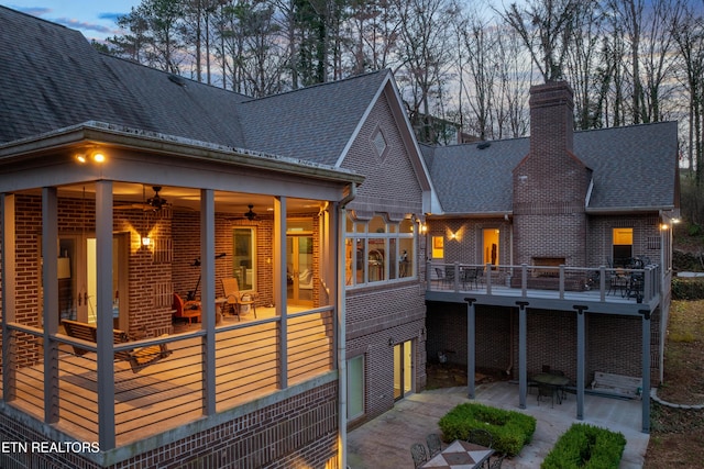 rear view of property featuring a ceiling fan, a patio, roof with shingles, a wooden deck, and brick siding