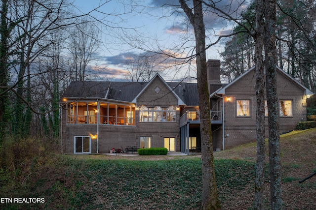 back of property at dusk featuring stairs, brick siding, a sunroom, and a chimney