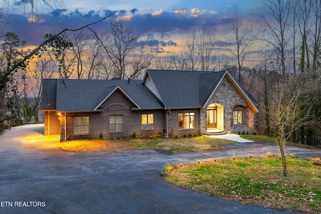 view of front of home featuring brick siding, driveway, and roof with shingles