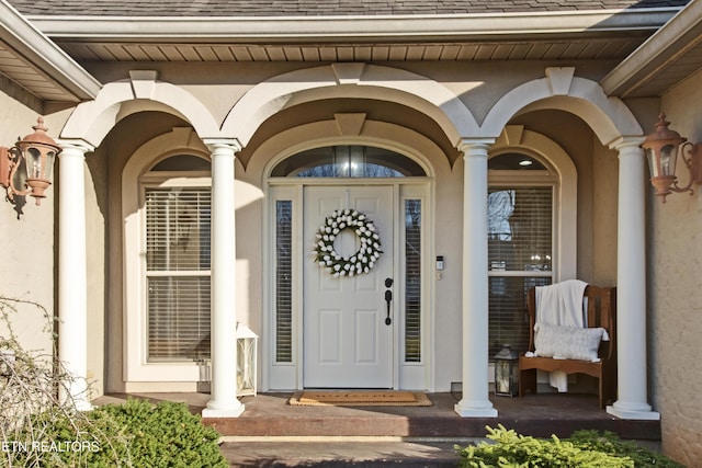 view of exterior entry featuring a shingled roof and stucco siding