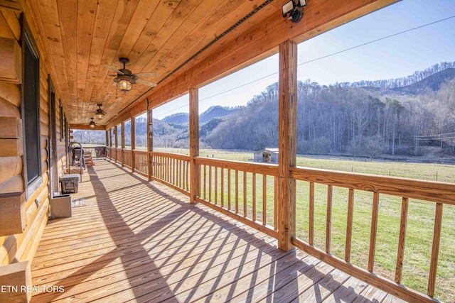 deck with ceiling fan, a lawn, a wooded view, and a mountain view