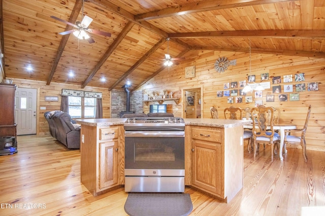 kitchen with vaulted ceiling with beams, light wood-style floors, open floor plan, stainless steel range with gas cooktop, and a wood stove