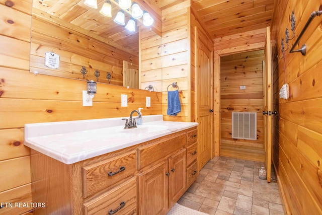 bathroom with visible vents, wooden ceiling, stone finish flooring, vanity, and wood walls