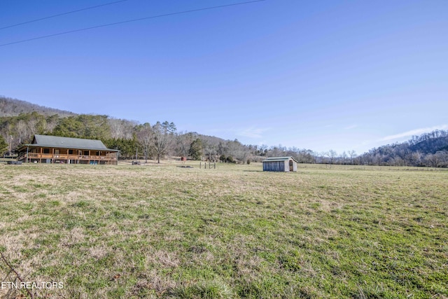 view of yard featuring a rural view, an outdoor structure, a wooded view, and a storage unit