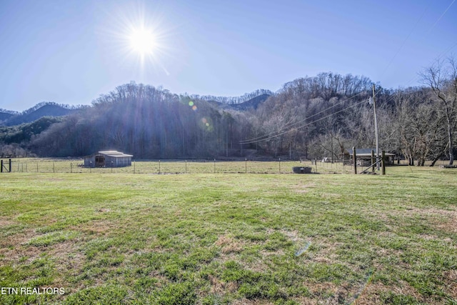 view of yard with a rural view, fence, a wooded view, and a mountain view