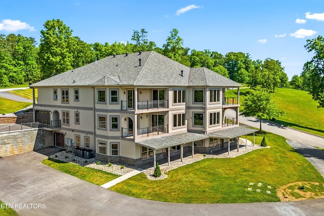 rear view of property featuring an attached garage, a balcony, driveway, a yard, and stucco siding