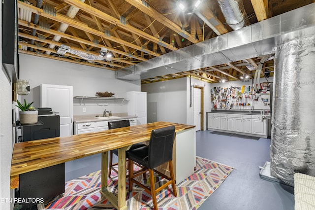 kitchen with open shelves, a sink, white cabinets, wooden counters, and concrete flooring