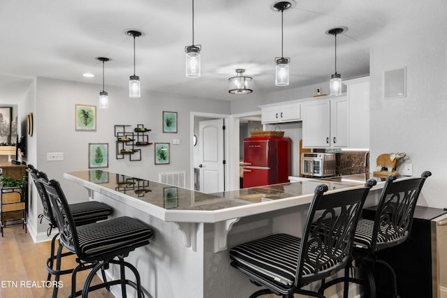 kitchen featuring visible vents, a breakfast bar, freestanding refrigerator, and light wood-style floors