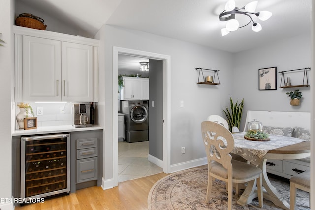 dining area with baseboards, washer / dryer, light wood-style flooring, wine cooler, and a chandelier