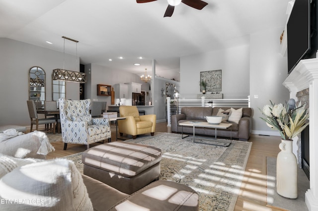 living room with wood finished floors, lofted ceiling, recessed lighting, a fireplace with raised hearth, and ceiling fan with notable chandelier