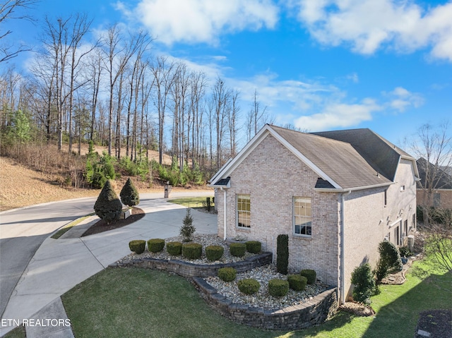 view of side of property with a yard, brick siding, and driveway