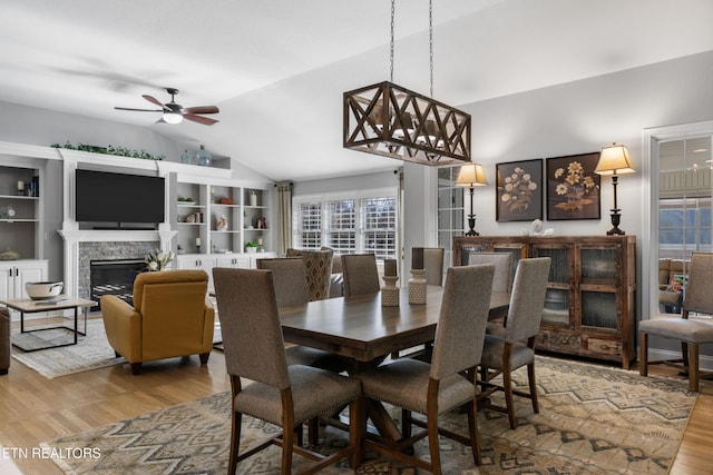 dining space featuring ceiling fan with notable chandelier, a fireplace, lofted ceiling, and wood finished floors