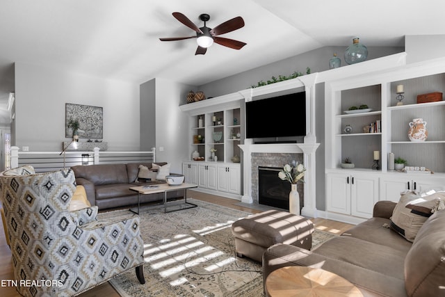 living area featuring a stone fireplace, ceiling fan, light wood-style floors, and vaulted ceiling