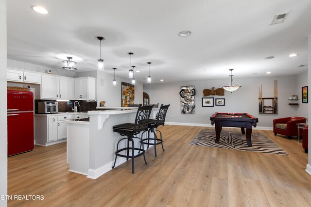 kitchen with visible vents, pool table, a breakfast bar area, light wood-type flooring, and fridge