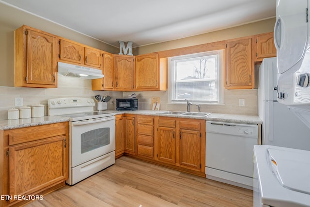 kitchen featuring light wood-style flooring, under cabinet range hood, a sink, tasteful backsplash, and white appliances