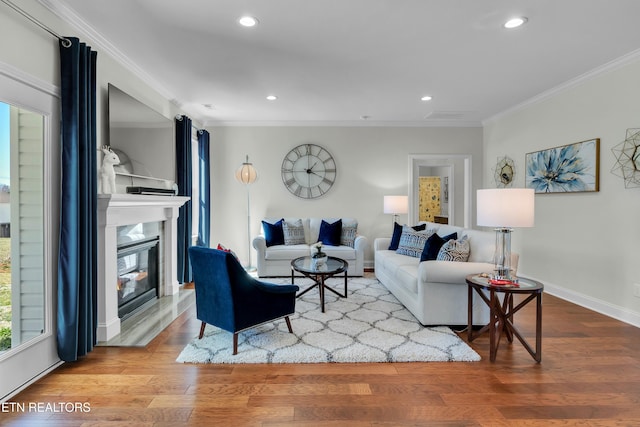 living room featuring baseboards, a glass covered fireplace, ornamental molding, wood finished floors, and recessed lighting