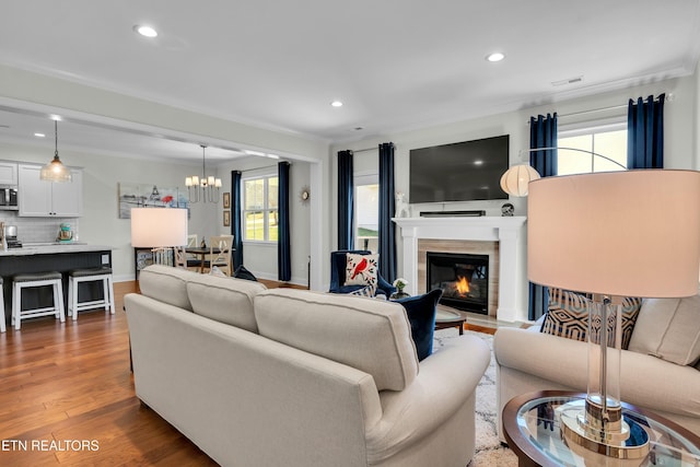 living room with crown molding, visible vents, a glass covered fireplace, wood finished floors, and a chandelier