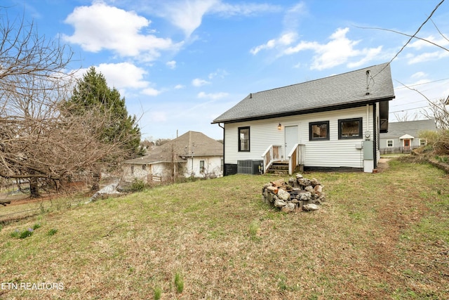 back of property with a yard, cooling unit, and a shingled roof