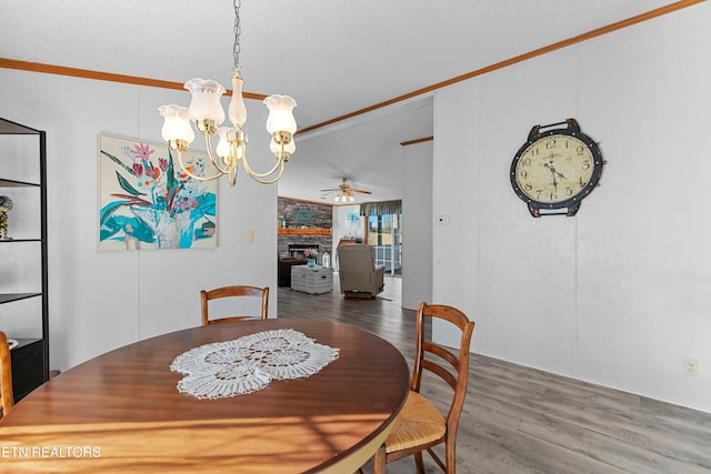 dining room with crown molding, a fireplace, a textured ceiling, wood finished floors, and ceiling fan with notable chandelier