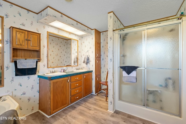 full bathroom with wallpapered walls, a textured ceiling, wood finished floors, and a shower with shower door