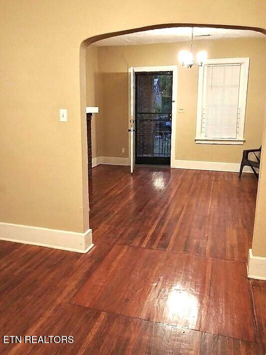 empty room featuring arched walkways, dark wood-type flooring, a chandelier, and baseboards