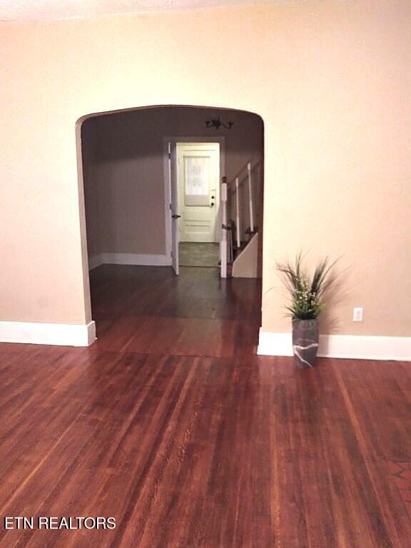 empty room with stairs, arched walkways, baseboards, and wood finished floors