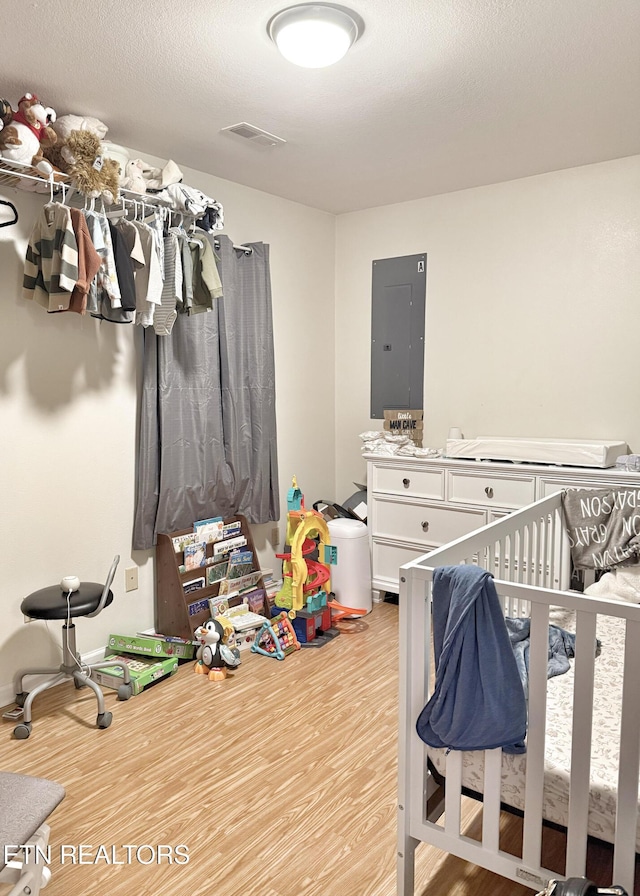 bedroom with light wood-style floors, electric panel, visible vents, and a textured ceiling