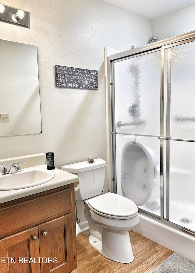 bathroom with a stall shower, vanity, toilet, and wood finished floors