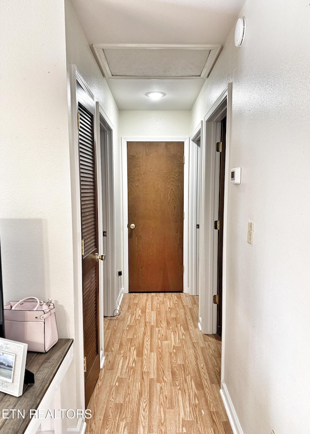 hall with attic access, light wood-type flooring, and baseboards