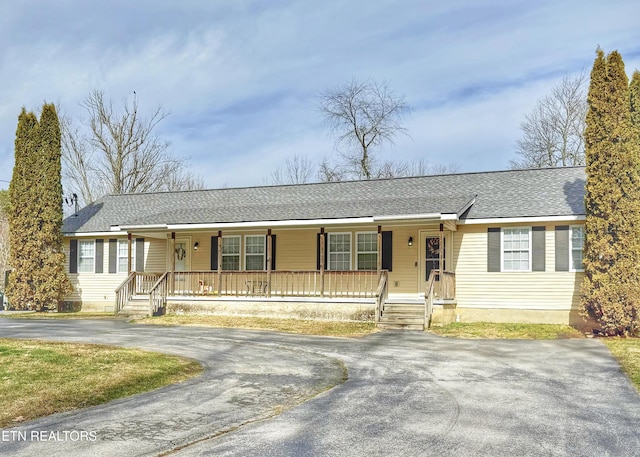 ranch-style home featuring covered porch, aphalt driveway, and roof with shingles